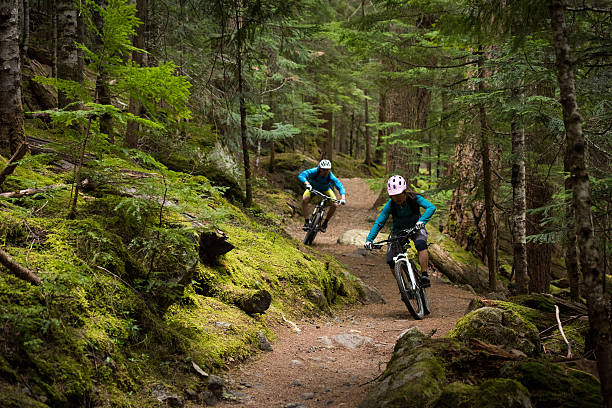 couple, faire du vélo de montagne dans une forêt - sports extrêmes photos et images de collection