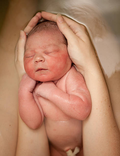 Mother's Arms Holding Newborn After Water Birth At Home Color photo of a loving mother's arms holding her newborn baby son in the water of a birthing tub after a water birth at home. water birth stock pictures, royalty-free photos & images