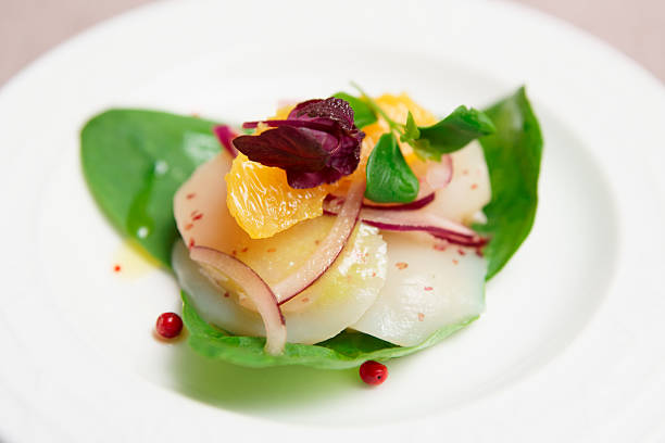 Sea scallop carpaccio with orange and herbs in plate, close-up