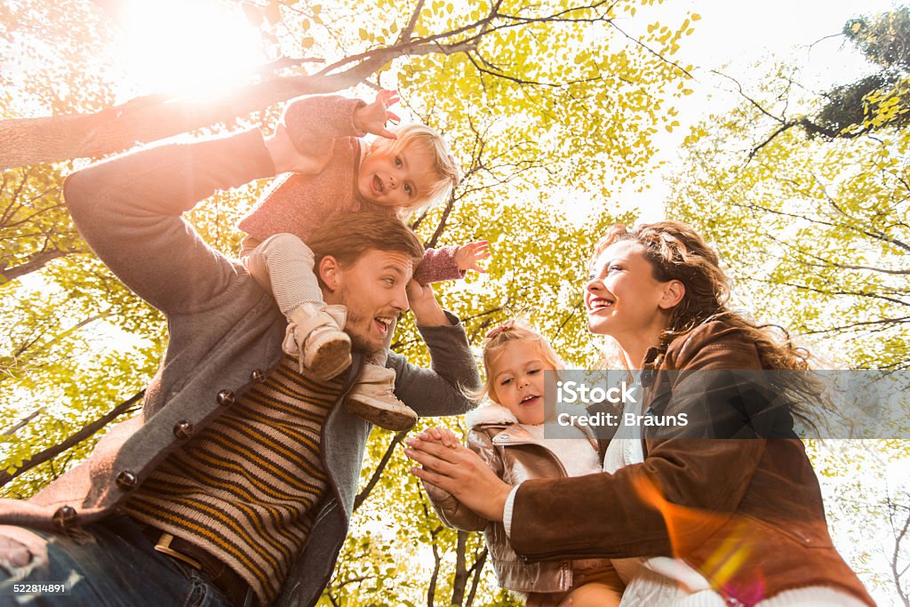 Family having fun in nature. Low angle view of happy young parents having fun with their little girls in the forest and enjoying in autumn day. Autumn Stock Photo
