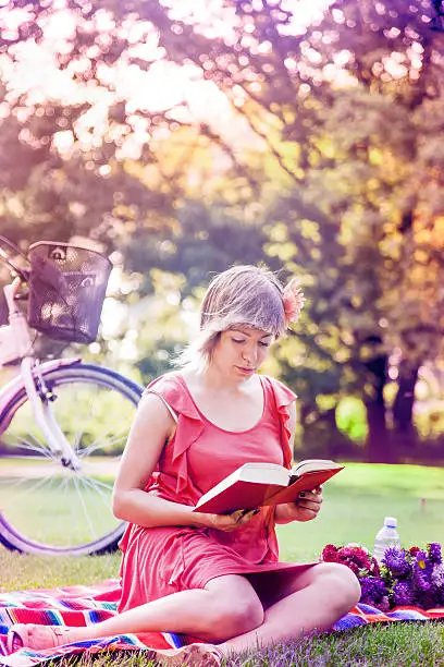 Beautiful countrygirl sitting on grass on a blanket, reading a book and enjoying sunny day.