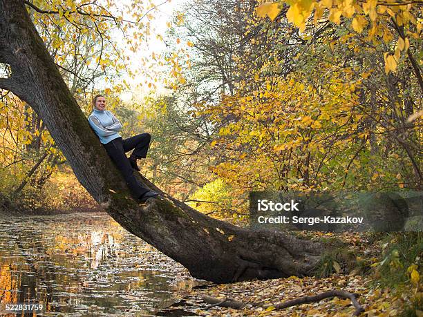 Young Woman Stands On A Tree And Smiling Stock Photo - Download Image Now - Adult, Adults Only, Autumn