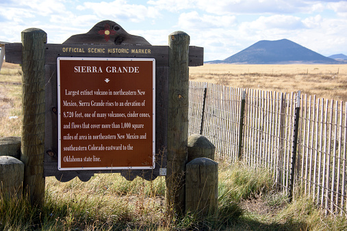 Historical marker in New Mexico of Sierra Grande, with the Capulin extinct volcano in the background. The scene includes bright, grassy prairie lands in the Great Plains of the New Mexico high desert.