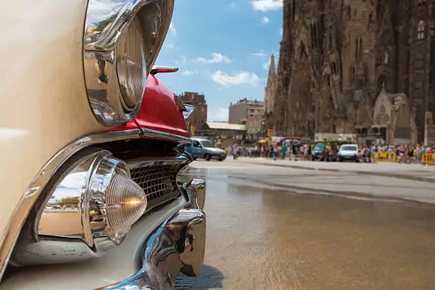 American vintage, detail of bumper and headlights. In the background stands the Sagrada Familia church in Barcelona flooded by broken piping. Spain