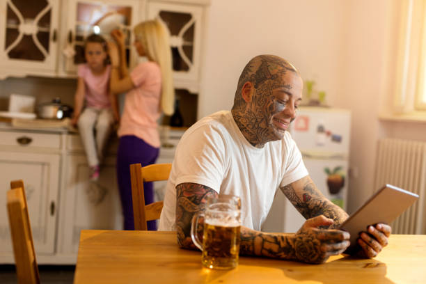 sonriente hombre tatuada con panel táctil en la cocina. - glass drink alcohol red fotografías e imágenes de stock