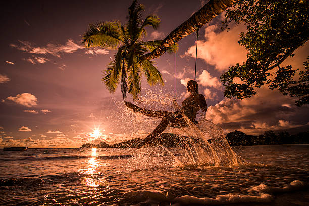 Happy woman having fun on a swing above the sea. Low angle view of young woman splashing water while swinging on a sunset beach. sunset beach hawaii stock pictures, royalty-free photos & images