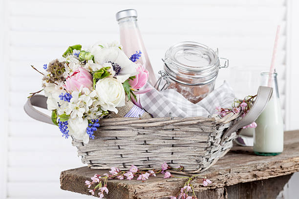 Sweet, rustic picnic basket with milk and flowers Bouquet from pink tulips, violet grape hyacinths, white anemones, violet veronica and white buttercup with violet ribbon lying in the picnic basket with milkshake in the bottle and sweets in the jar with white background and the old wooden bench grape hyacinth photos stock pictures, royalty-free photos & images