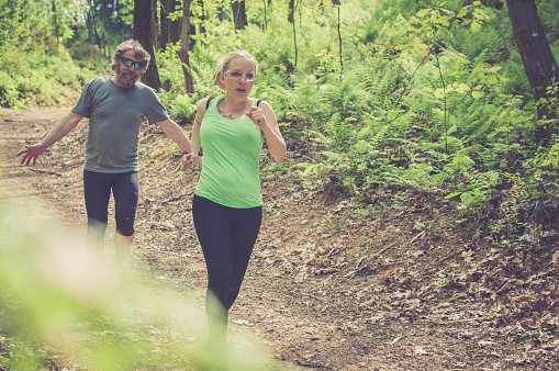 Young blonde caucasian woman and elderly man with a beard running in the forest; outdoor sport photography, all logos removed.