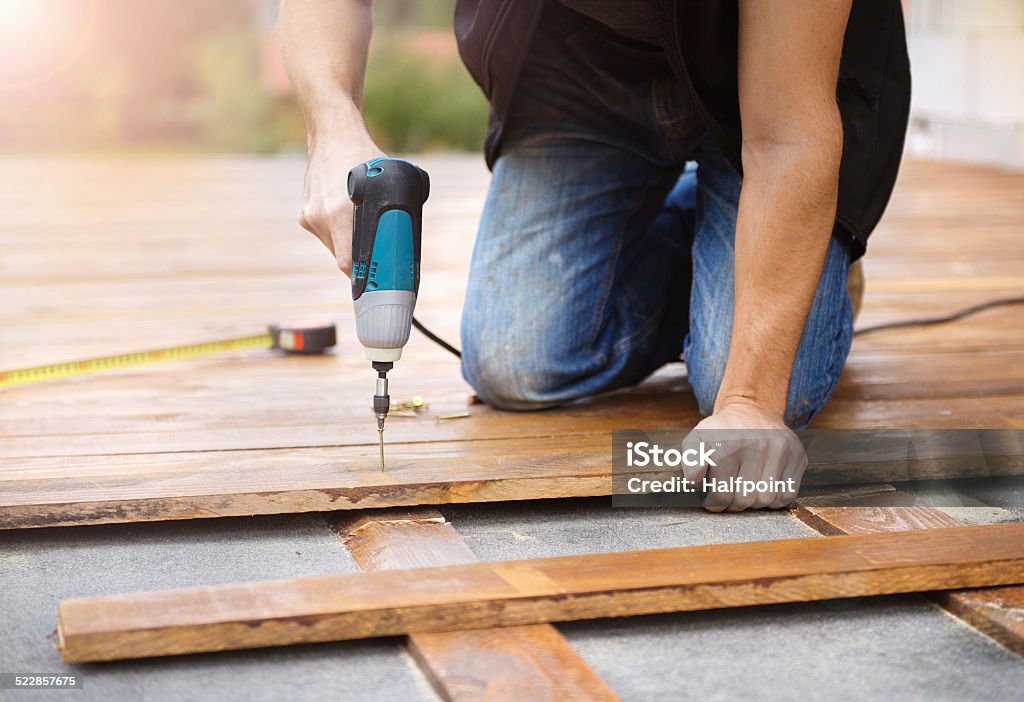 Handyman installing wooden flooring Handyman installing wooden flooring in patio, working with drilling machine Installing Stock Photo