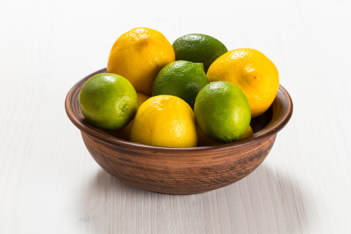 Lemons and limes in a clay bowl on white wooden table