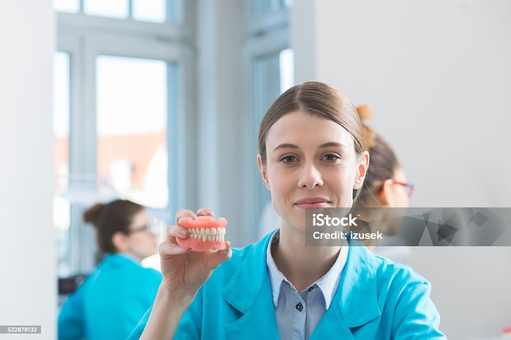Female students learning prosthetic dentistry Female students in a prosthodontic lab, learning prosthetic dentistry. Focus on smiling girl holding dentures in hand and smiling at camera. Education Stock Photo