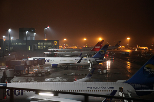Frankfurt, Germany - January 23, 2011: Passenger aircrafts of different international airlines are being prepared and boarded for their flights at the stationary parking positions at Frankfurt Airport, Germany during snowfall at night. Snow and visible ice on the wings is not a problem for airplanes. Right after being towed into taxiing position they are de-iced by the airport service crew.