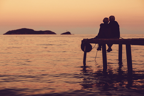 Loving senior couple enjoying the sunset, sitting on the dock