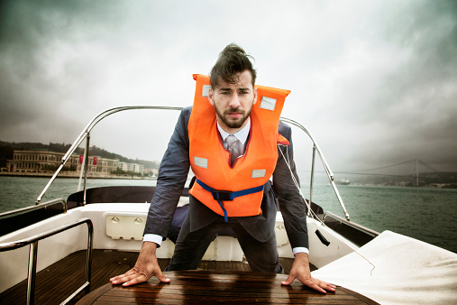 Concerned businessman at sea during a storm looking at camera with a, intense, serious expression. He is wearing a life jacket and is trying to keep collected.