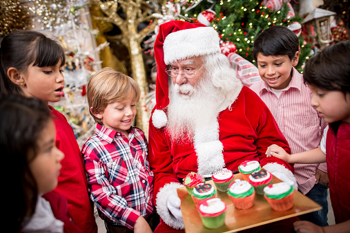 Santa giving Christmas cupcakes to a group of kids