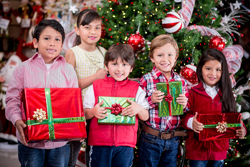 Group of kids holding Christmas presents next to the tree