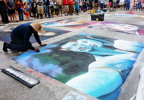 Lake Worth, Florida, USA - February 23, 2014: An artist works on a chalk painting at the Lake Worth Street Painting Festival. The festival features hundreds of artists who cover the streets with chalk paintings. Dozen of spectators are partially visible in the background.