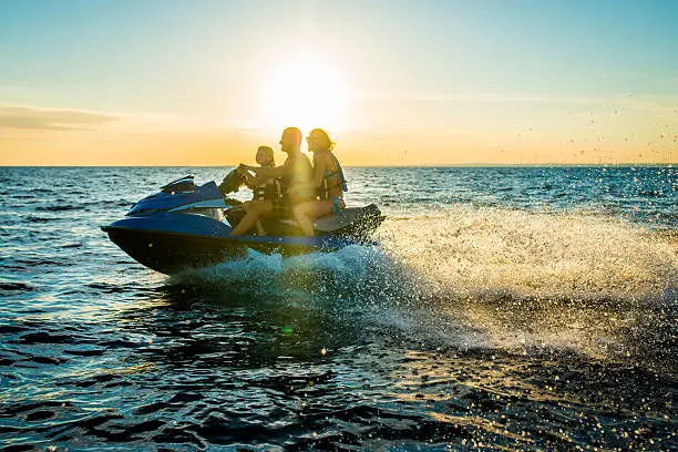 Family having fun riding a person watercraft/water scooter on the sea in the sunset.  