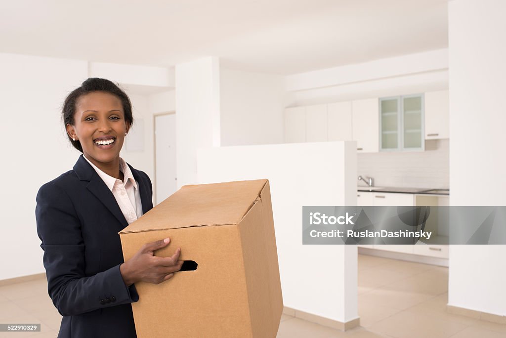 Woman moving home. Smiling young business woman moving home, holding cardboard box. African Ethnicity Stock Photo