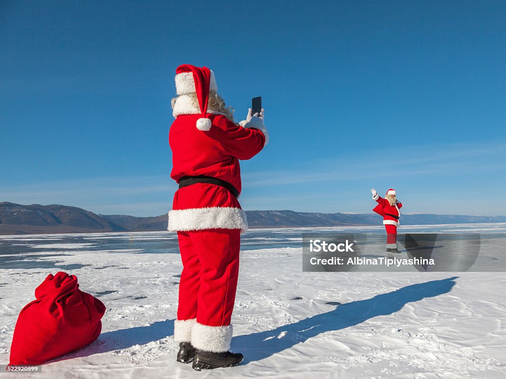 Santa Claus shoot on a smartphone of other SantaClaus Santa Claus shoot on a smartphone of other Santa, walking on the snow,  multiexposition, shooting was conducted in a sunny day on lake Baikal Active Seniors Stock Photo