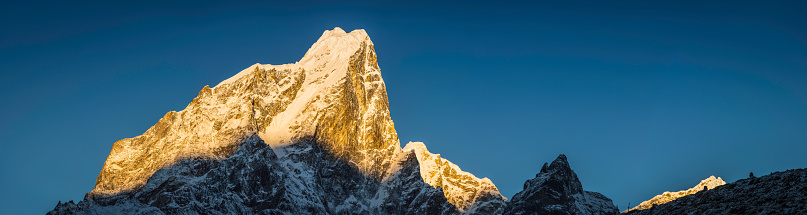 Golden light of daybreak illuminating the snow capped summit and dramatic rocky pinnacles of Taboche (6495m) glowing against the blue high altitude skies of the Sagarmath National Park, a UNESCO World Heritage Site deep in the Himalaya mountains of Nepal. ProPhoto RGB profile for maximum color fidelity and gamut.