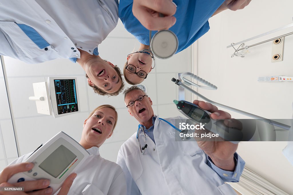 doctors and surgeon checking on patient low angle view on male doctor, male nurse, female doctor and female surgeon in blue scrubs checking on patient in hospital, hart rate monitor on the ceiling Bed - Furniture Stock Photo