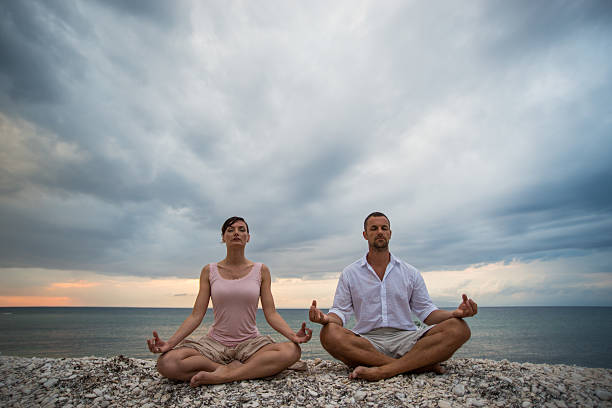 zwei personen tun yoga am strand - zen like nature breathing exercise sitting stock-fotos und bilder