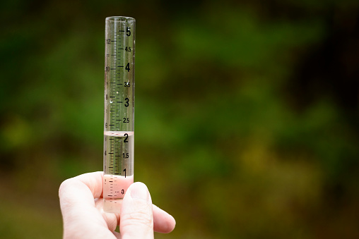 A hand holding a glass rain gauge so that the latest precipitation data can be gathered.