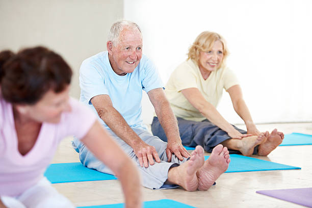 Staying fit and active Shot of a group of smiling seniors enjoying a yoga class touching toes stock pictures, royalty-free photos & images