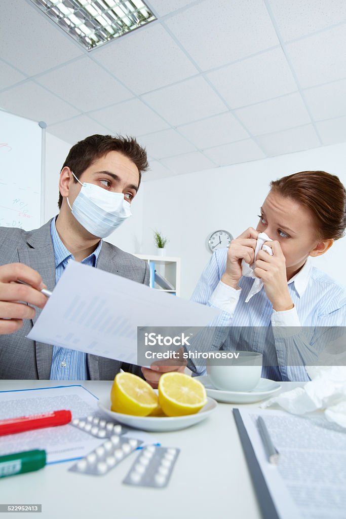 Discussion Image of man in mask looking at his sick business partner while discussing papers in office Adult Stock Photo