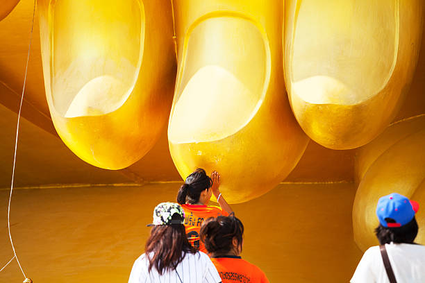 Ang Thong - November 12, 2014: Capture of some thai girls and teens standing close to large buddhe of Wat Muang in Ang Thong, close to Ayutthaya. A girl is placing hands and head at huge finger. Buddha is 95 m high and 63 m wide.