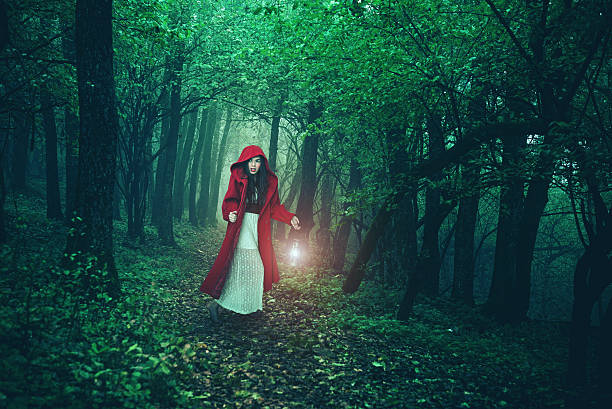 girl with bright red wavy hair sanding with back to camera, lady in green cloak and white dress stretches, morning of fairy-tale princess in forest, bright orange light of the sun through fog.