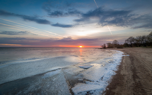 Sunset at frozen bay. Ice on the water and sand beach line