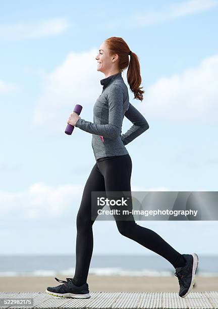 Photo libre de droit de Heureuse Jeune Femme Jogging Avec Poids Et Haltères banque d'images et plus d'images libres de droit de Marche sportive