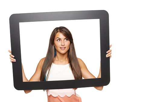 Smiling young woman looking to side through tablet frame, over white background