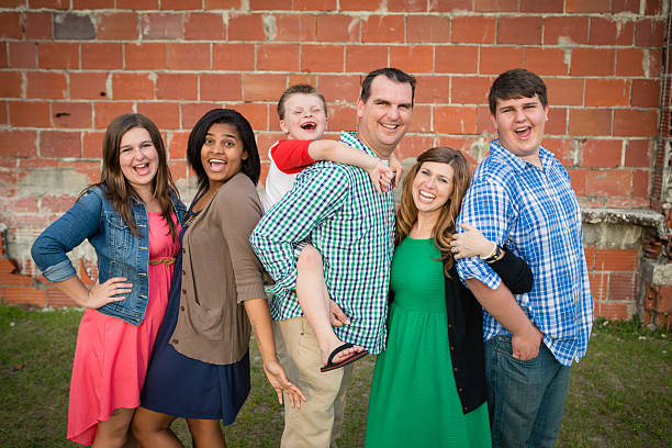 Happy Family of Six Together with Adopted Daughter Color photo of a happy husband and wife laughing with their biological sons and daughter and adopted daughter while standing outside together. 13 14 years child teenage girls lying down stock pictures, royalty-free photos & images