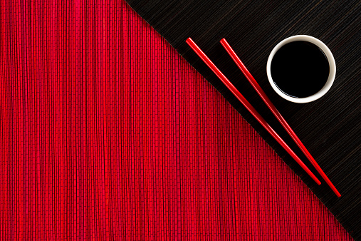 Chopsticks and bowl with soy sauce on bamboo mat