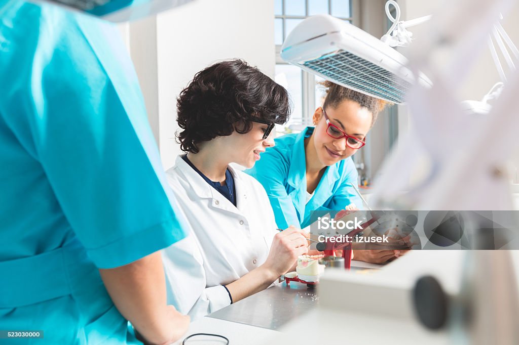 Multi ethnic female students learning prosthetic dentistry Multi ethnic female students wearing uniforms in a prosthodontic lab, learning prosthetic dentistry. Afro american woman talking with teacher. Dental Health Stock Photo