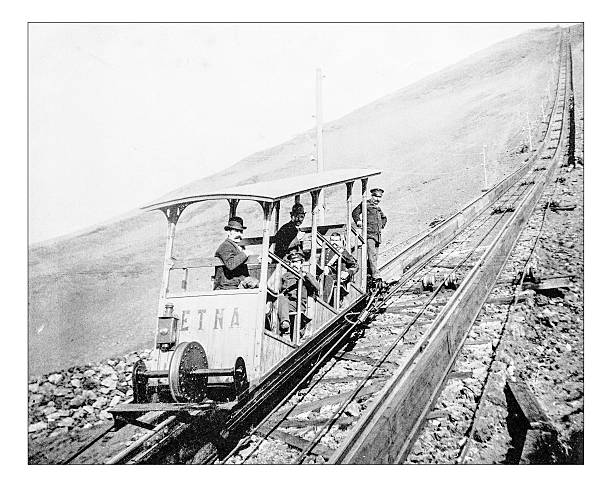 Antique photograph of ascent of Mont Vesuvius by funicular railway during the 19th century. The railway was built after 1878 to connect Ercolano (Naples) to the area just below the crater of Vesuvius Volcano. In the picture one of the two coaches, the one called Etna (named after the other famous Italian volcano), with its passengers and the driver. Behind them the rails go up towards the top of the mountain (19th century Stereoscopy