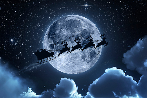 Santa flying in his sleigh against a full moon background with stars and clouds.