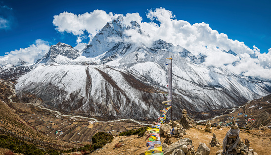 Colourful Buddhist prayer flags fluttering in the breeze above the Sherpa village of Dingboche, overlooked by the iconic snowy spire of Ama Dablam (6812m) deep in the Himalaya mountains of the Everest National Park, a UNESCO World Heritage Site, Nepal. ProPhoto RGB profile for maximum color fidelity and gamut.