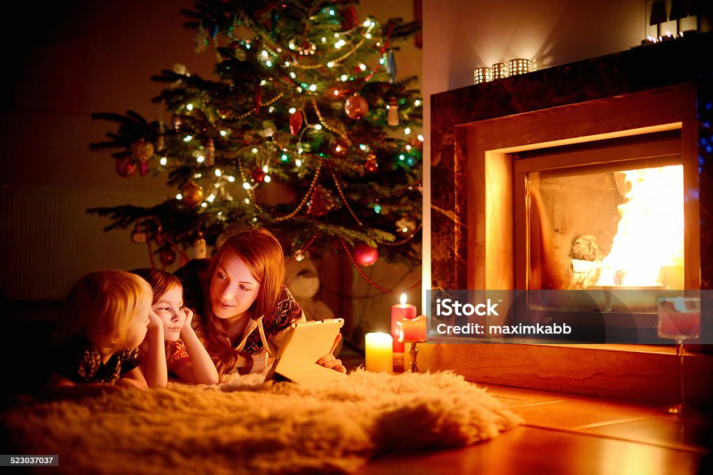 Young mother and her daughters using a tablet pc Young mother and her daughters using a tablet pc by a fireplace on warm Christmas evening Fire - Natural Phenomenon Stock Photo