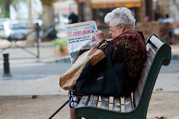 ILL`Rousse, Corsica, France, October 8, 2010: Elderly woman sitting on a local city bench an reading the newspapper 