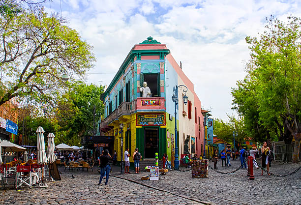 Colorful Building La Boca, Buenos Aires, Argentina Buenos Aires, Argentina - April 15, 2015: The main square on of the Camanito in the La Boca neighborhood of Buenos Aires features brightly colored buildings and cobblestone streets that are a popular tourist destination. Tourists can be seen surrounding the most recognizable building the the neighborhood at the center of the square. The area is a popular destination for watching tango dancers in the street, shopping for souvenirs handicrafts made by local artisans and restaurants. It is the oldest neighborhood in Buenos Aires and is located at the mouth of the port, which gives it its namesake.  la boca buenos aires stock pictures, royalty-free photos & images