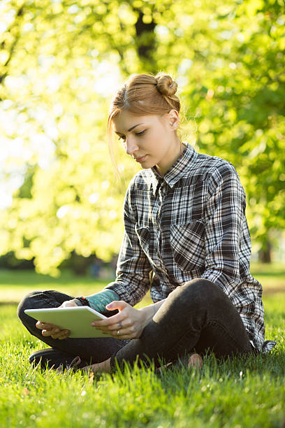 istock woman sitting on grass in park and using digital tablet 523041770