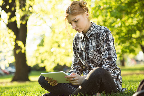 istock woman sitting on grass in park and using digital tablet 523041860