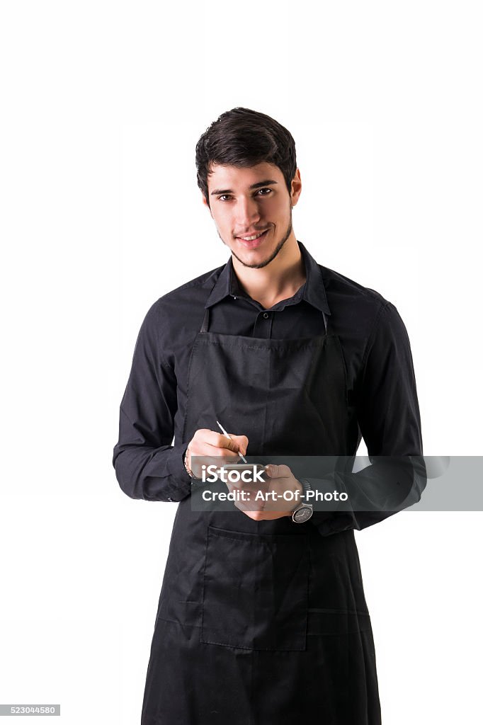 Full length shot of young chef or waiter posing isolated Full length shot of young chef or waiter posing, wearing black apron and shirt, writing order electronic device, isolated on white background Waiter Stock Photo