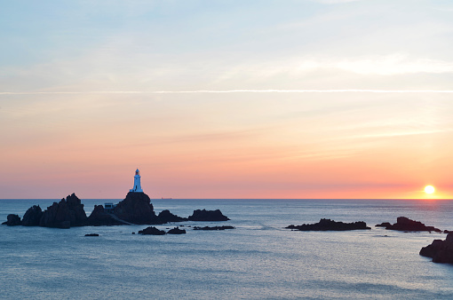 Corbiere Lighthouse on Jersey in the Channel Islands. Image taken at sunset just at the moment as the sun is slipping over the horizon. Also visible, between the lighthouse and the sun, is a tanker passing from left to right through the image.