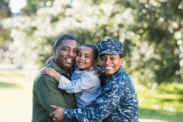 Military homecoming, navy servicewoman with family A military homecoming. Portrait of an African American woman wearing navy camouflage uniform standing outdoors with her family. Her husband is holding their 5 year old son who is in the middle between his parents, smiling at the camera. The main focus is on the woman. black military man stock pictures, royalty-free photos & images