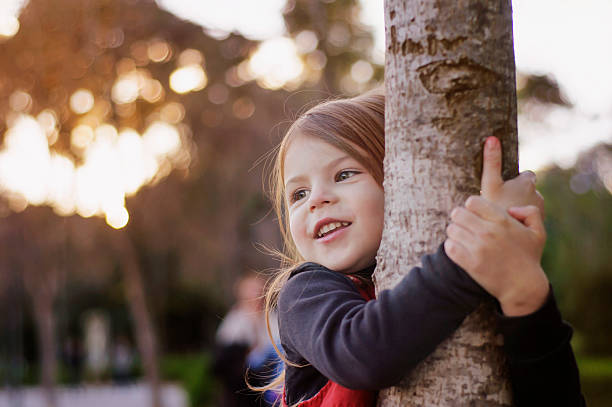 linda garotinha sorridente abraçando um tronco de árvore. - abraçar árvore - fotografias e filmes do acervo